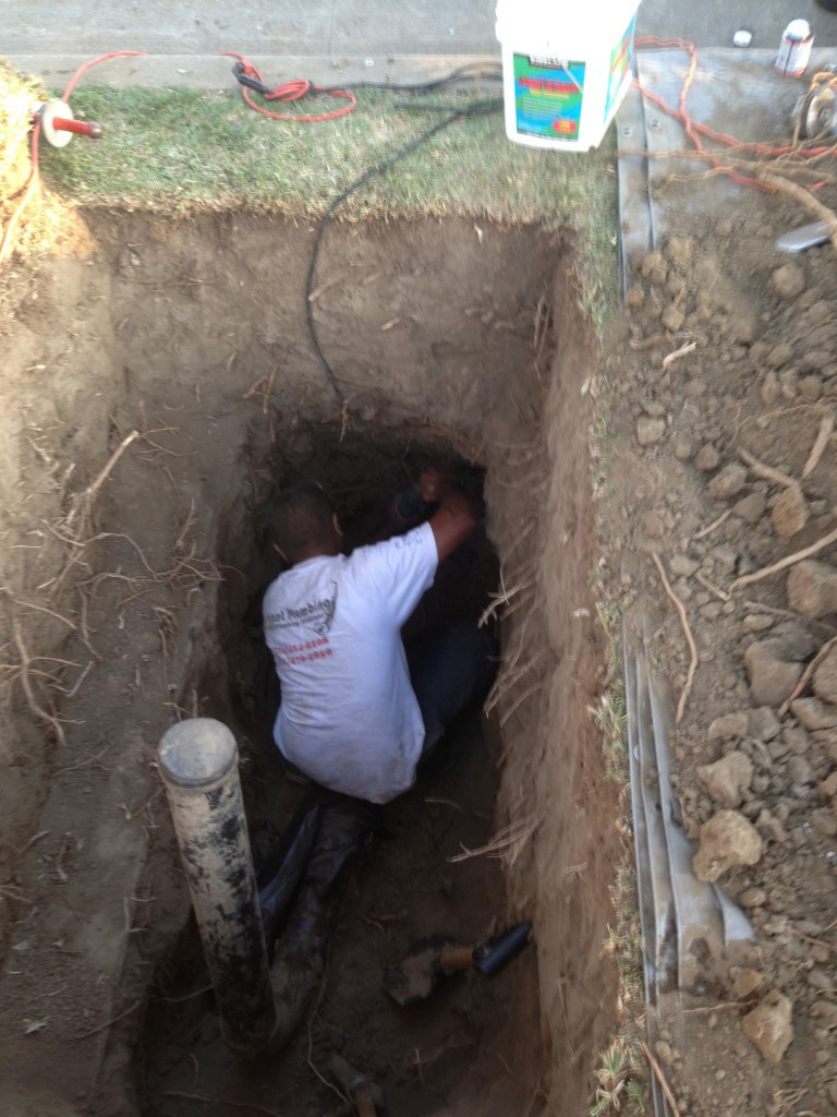 Worker in white shirt performing excavation work in deep trench