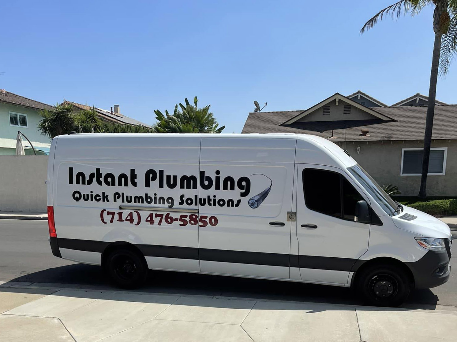 White plumbing service van with "Instant Plumbing" branding and phone number parked in residential driveway